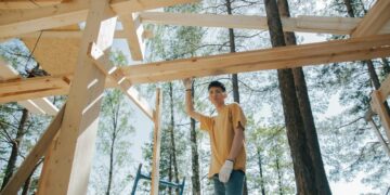 Asian man at a construction site building a wooden frame among trees.