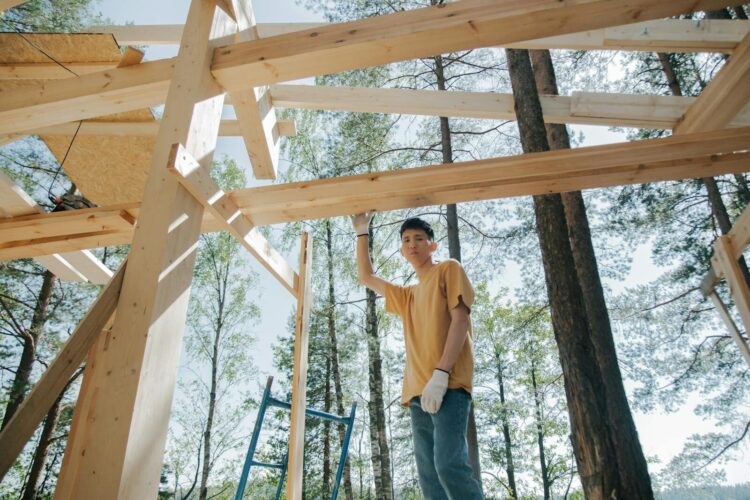 Asian man at a construction site building a wooden frame among trees.