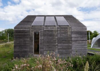 Sustainable wooden house with solar panels and lush surroundings.