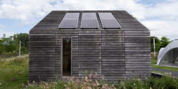 Sustainable wooden house with solar panels and lush surroundings.