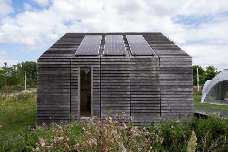 Sustainable wooden house with solar panels and lush surroundings.