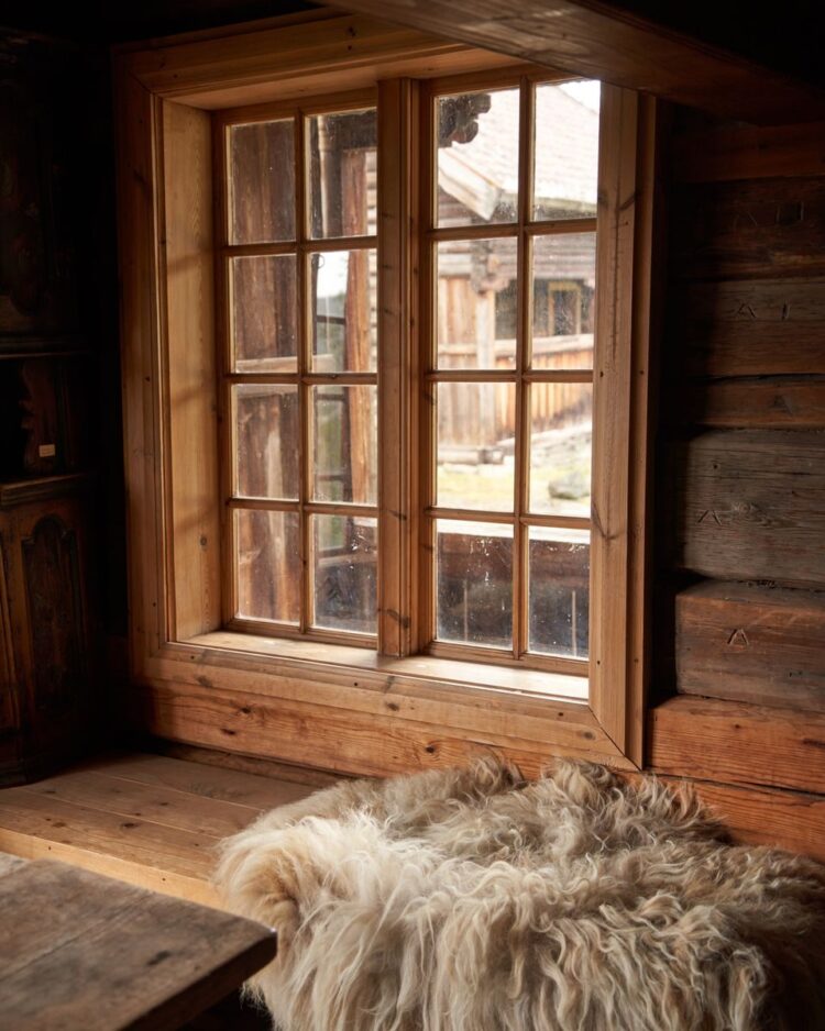 Warm rustic setting in a Norwegian log cabin, featuring a wooden window and sheepskin decor.