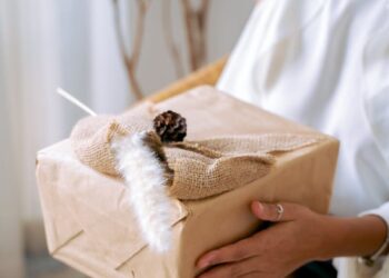 A joyful woman holding a beautifully wrapped natural gift in an indoor setting.