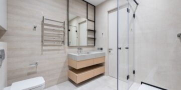 Interior of modern light bathroom with toilet and bidet next to bath and sink with faucet on cabinet under mirror