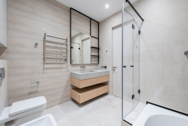Interior of modern light bathroom with toilet and bidet next to bath and sink with faucet on cabinet under mirror