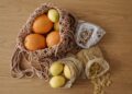 Eco-friendly grocery with fruits, pasta, and beans in reusable mesh bags on wooden surface.