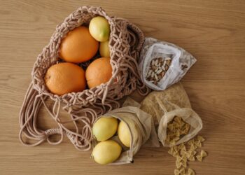 Eco-friendly grocery with fruits, pasta, and beans in reusable mesh bags on wooden surface.