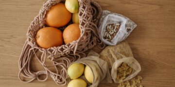 Eco-friendly grocery with fruits, pasta, and beans in reusable mesh bags on wooden surface.