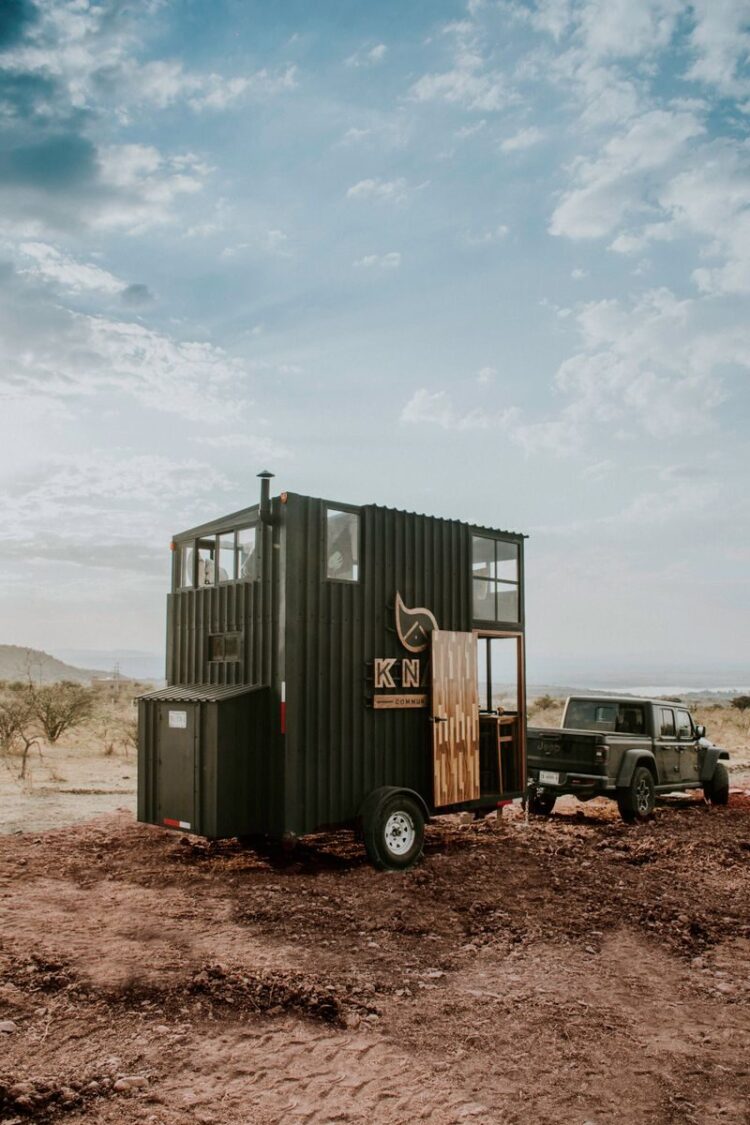An off-road vehicle towing a mobile trailer in a vast desert landscape under a cloudy sky.
