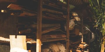Rustic outdoor storage area with logs and building materials, set in a sunny garden.