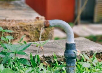 A flowing water pipe surrounded by lush green grass and a concrete platform in an outdoor setting.