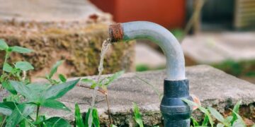 A flowing water pipe surrounded by lush green grass and a concrete platform in an outdoor setting.