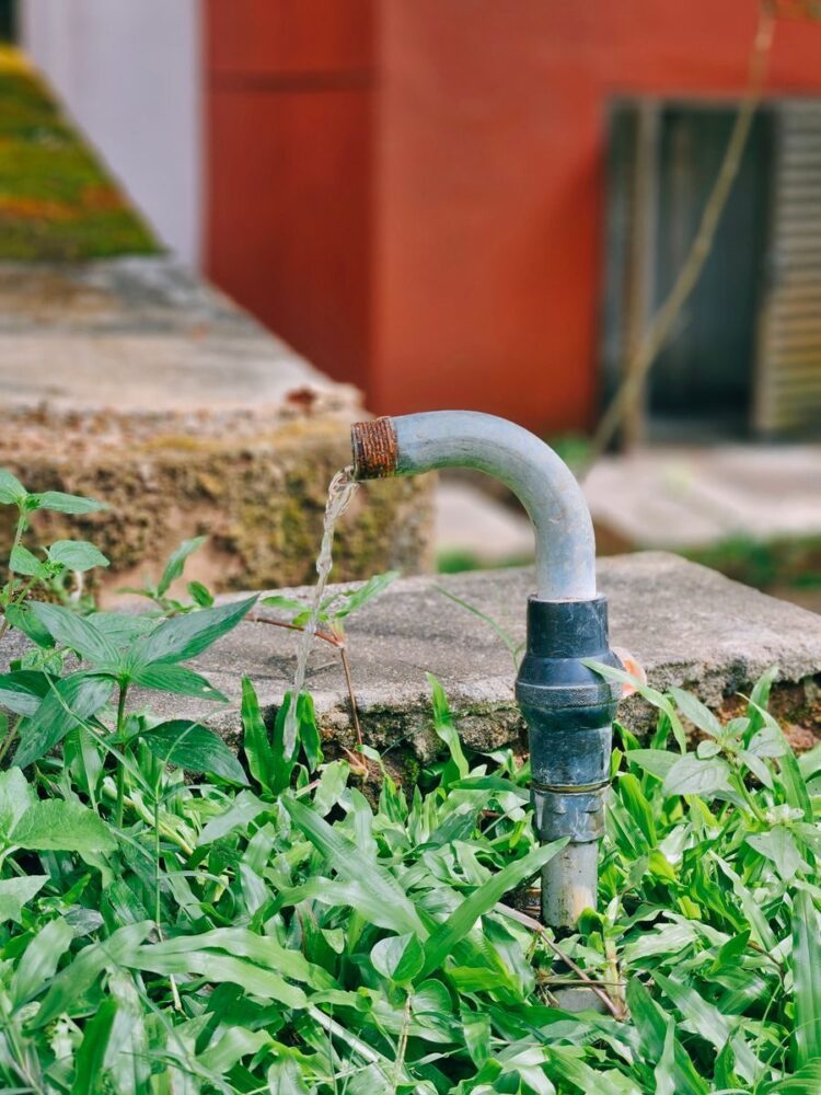 A flowing water pipe surrounded by lush green grass and a concrete platform in an outdoor setting.
