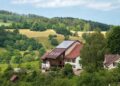 Idyllic farmhouse with solar panels surrounded by lush green fields and forests.