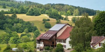 Idyllic farmhouse with solar panels surrounded by lush green fields and forests.