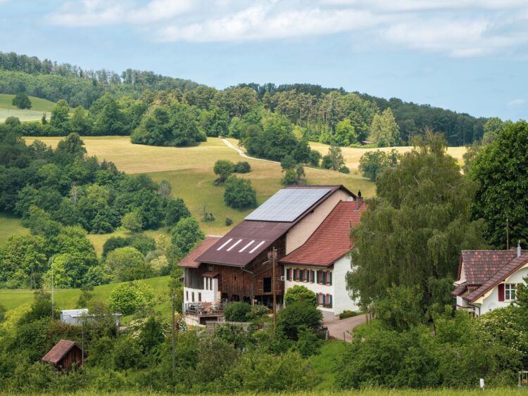 Idyllic farmhouse with solar panels surrounded by lush green fields and forests.